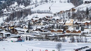 Ein verschneites Dorf mit traditionellen Holzhäusern, einer Kirche und einer Skipiste.