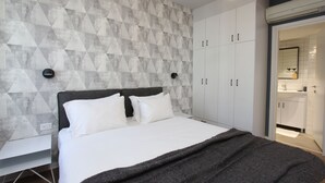 A modern bedroom with a geometric-patterned wall, a bed with white linens, and a dark throw blanket. - 1 BR Apt TLV TAU by Sea N' Rent (Tel Aviv)