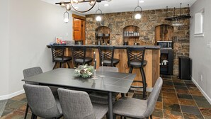 A modern kitchen with a stone backsplash, a central island with bar stools, and a dining area with a dark table and grey chairs. - Escape to Modern Mountain Retreat Near Top Ski Resorts w/ Hot Tub! (Gypsum)