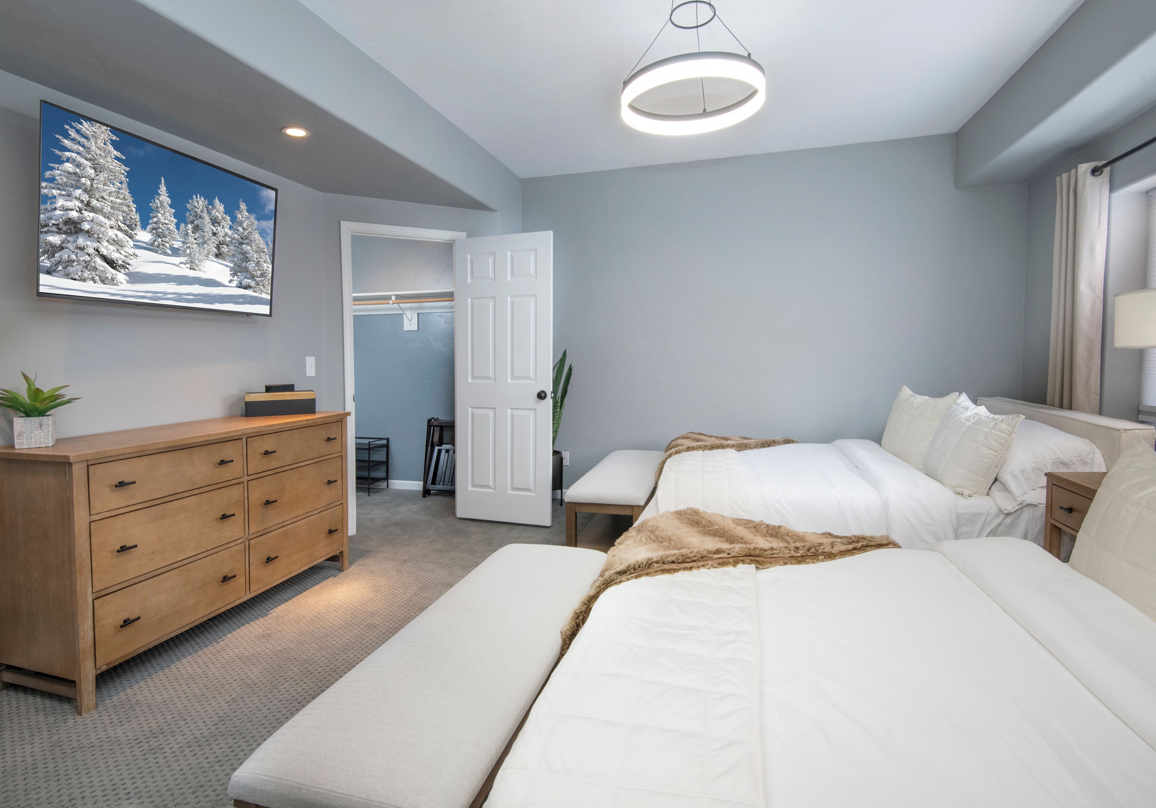 A bedroom with a bed, bedside tables, a dresser, a television, and a door leading to a bathroom.
