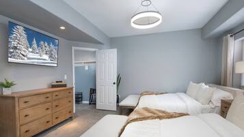 A bedroom with a bed, bedside tables, a dresser, a television, and a door leading to a bathroom.