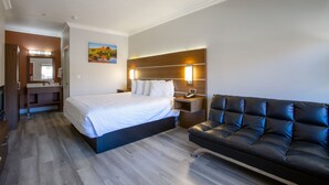 Quarto de hotel moderno com uma cama grande, um sofá de couro, uma cabeceira de madeira, uma mesa de cabeceira e um quadro na parede.