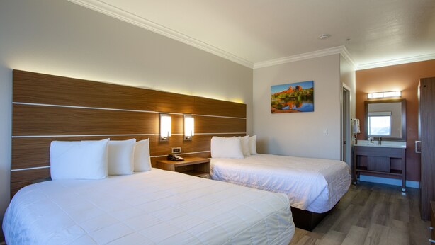 Habitación de hotel con dos camas, cabecero de madera, lámparas de noche, un cuadro en la pared y un baño con espejo y lavamanos.