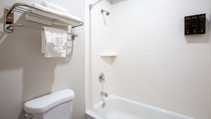 Un baño con inodoro blanco, bañera, toallero con toallas, cabezal de ducha y dispensador de jabón en la pared.