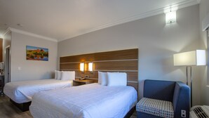 Habitación de hotel con dos camas, una mesita de noche con lámpara, una silla y un cuadro en la pared.
