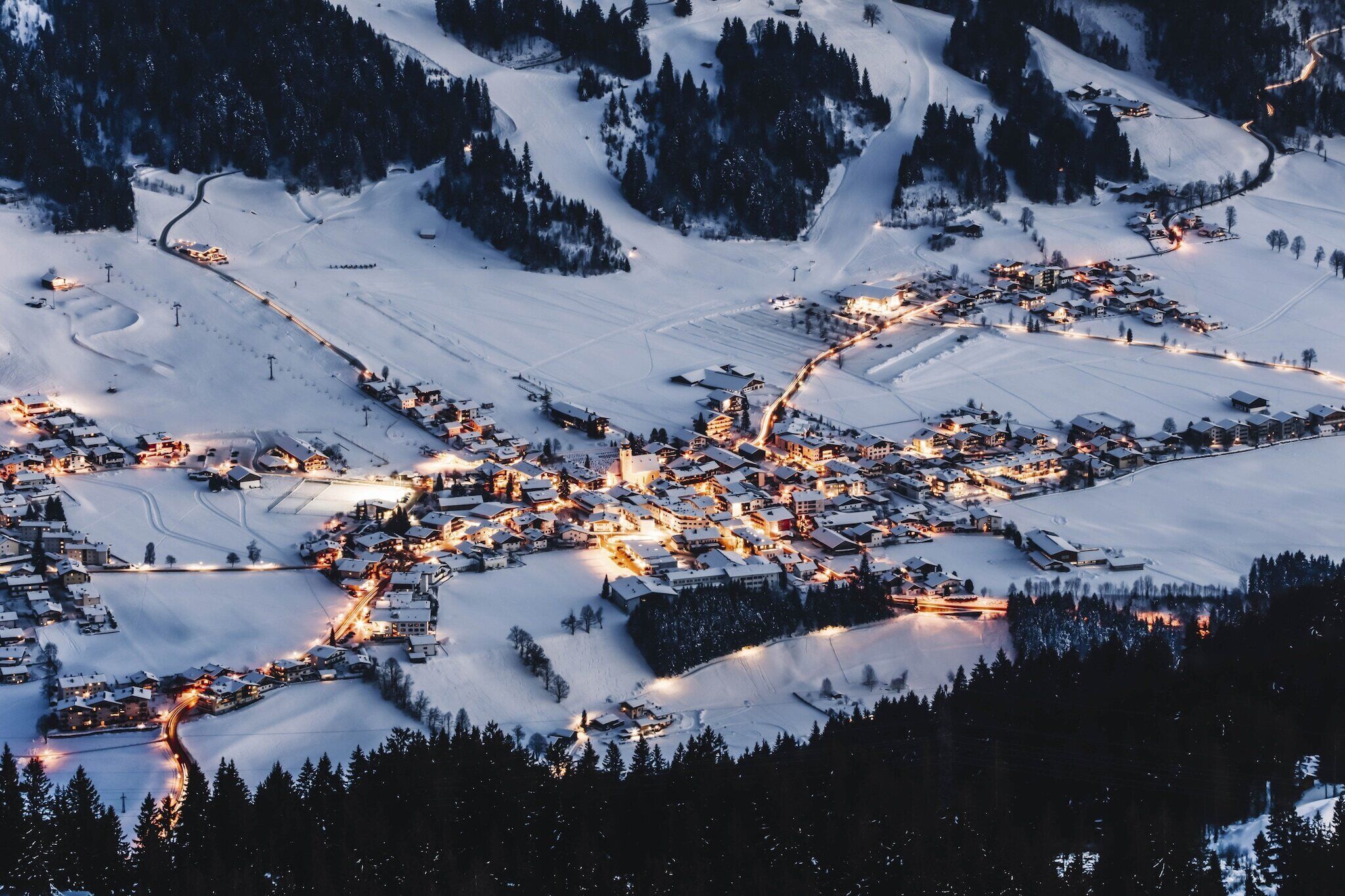A snow-covered village with illuminated buildings and winding roads.