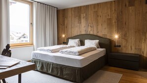 Une chambre avec un mur en bois, un lit avec une literie blanche, une table de chevet et une commode.