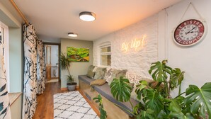 Un espace d’accueil avec un mur en pierre, un panneau lumineux au néon, une horloge et une grande plante.