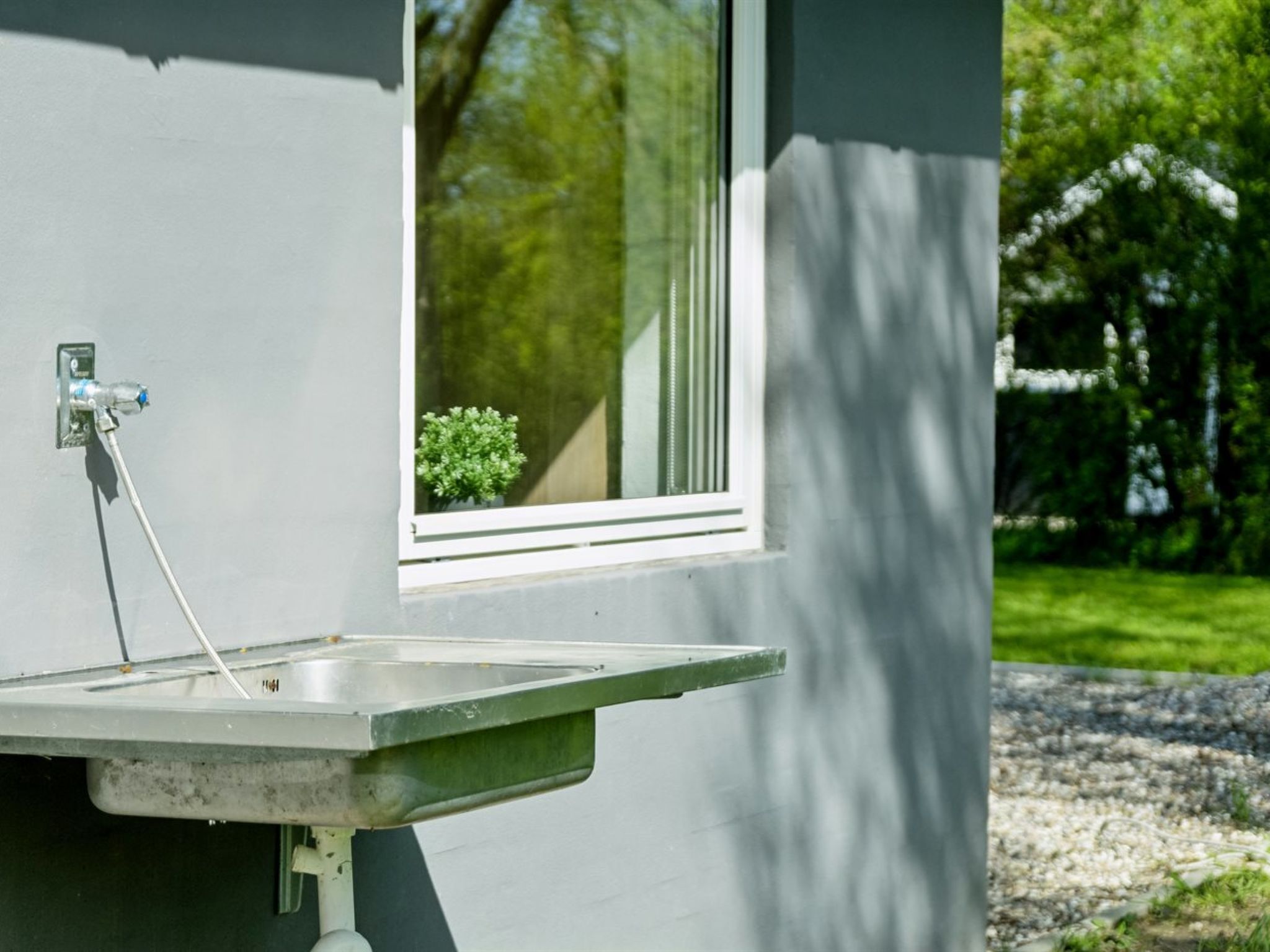 Une salle de bain avec un lavabo, une fenêtre et une petite plante visible à travers la fenêtre.