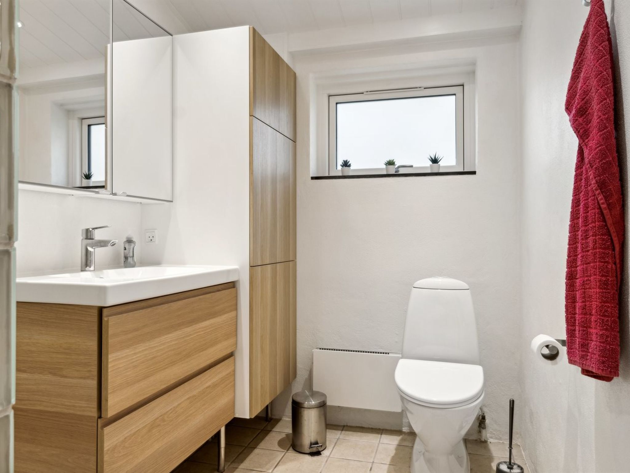 Ein modernes Badezimmer mit einem weißen Waschbecken, einem Holz-Waschtisch, einer Toilette und einem Fenster über dem Waschbecken.