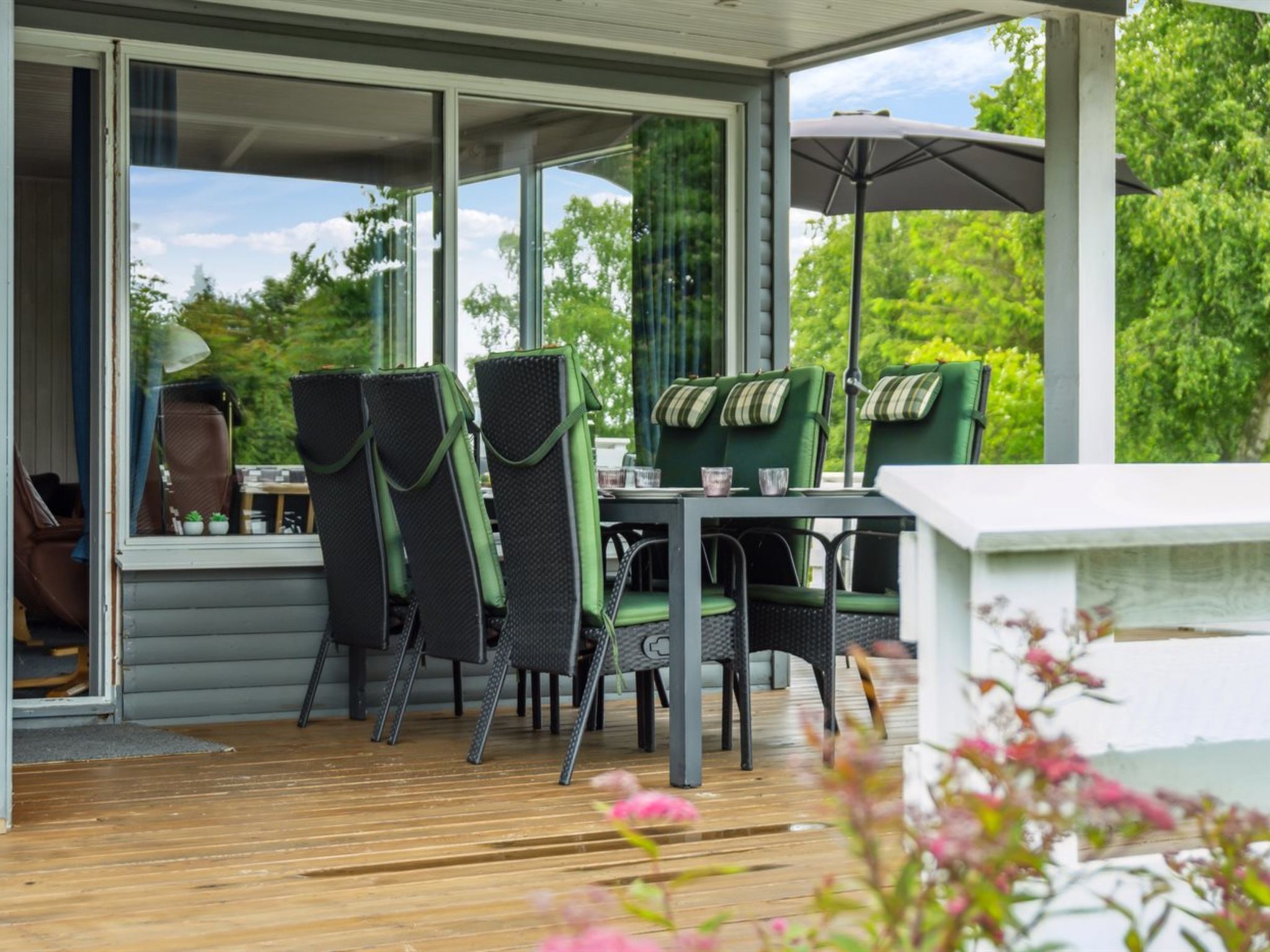 Une terrasse extérieure avec une table et des chaises, de grandes fenêtres et une vue sur la verdure.