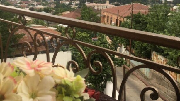 A balcony with a metal railing, a table with a cup of coffee, and a bouquet of flowers. - Spacious 4-bedroom house in charming Kutaisi with WiFi, AC (Kutaisi)