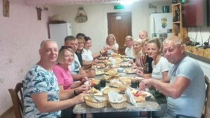 A group of people seated around a table with various dishes, in a room with wooden flooring and a pink wall. - Spacious 4-bedroom house in charming Kutaisi with WiFi, AC (Kutaisi)