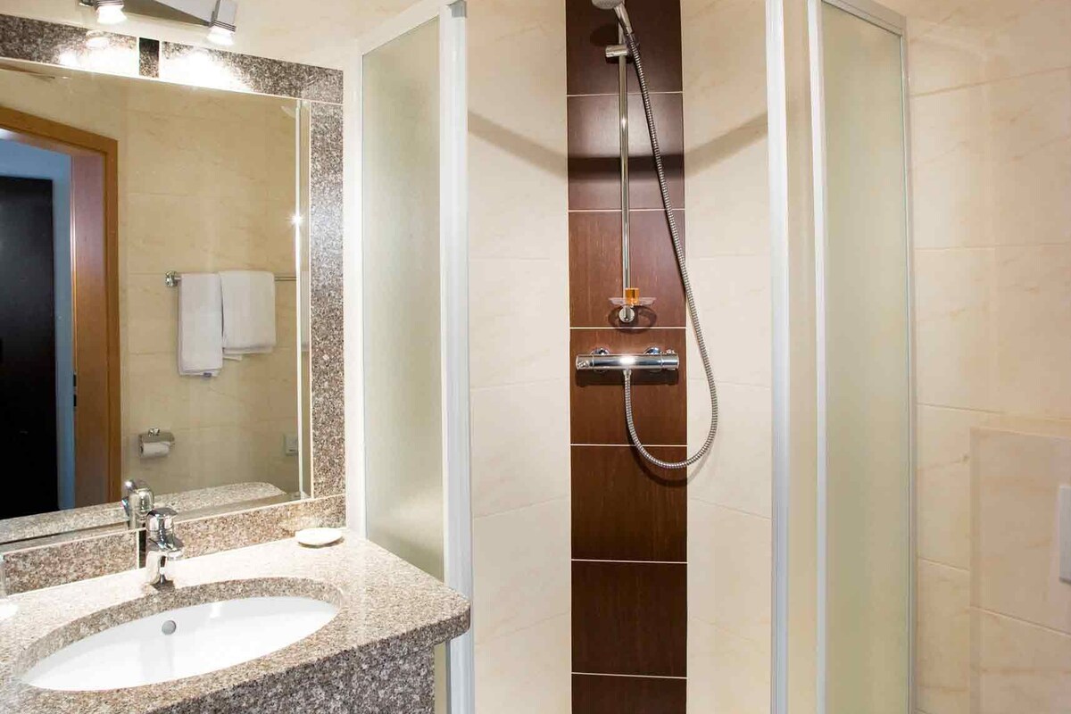 Un baño moderno con lavamanos de granito, ducha con mampara de vidrio y retrete.