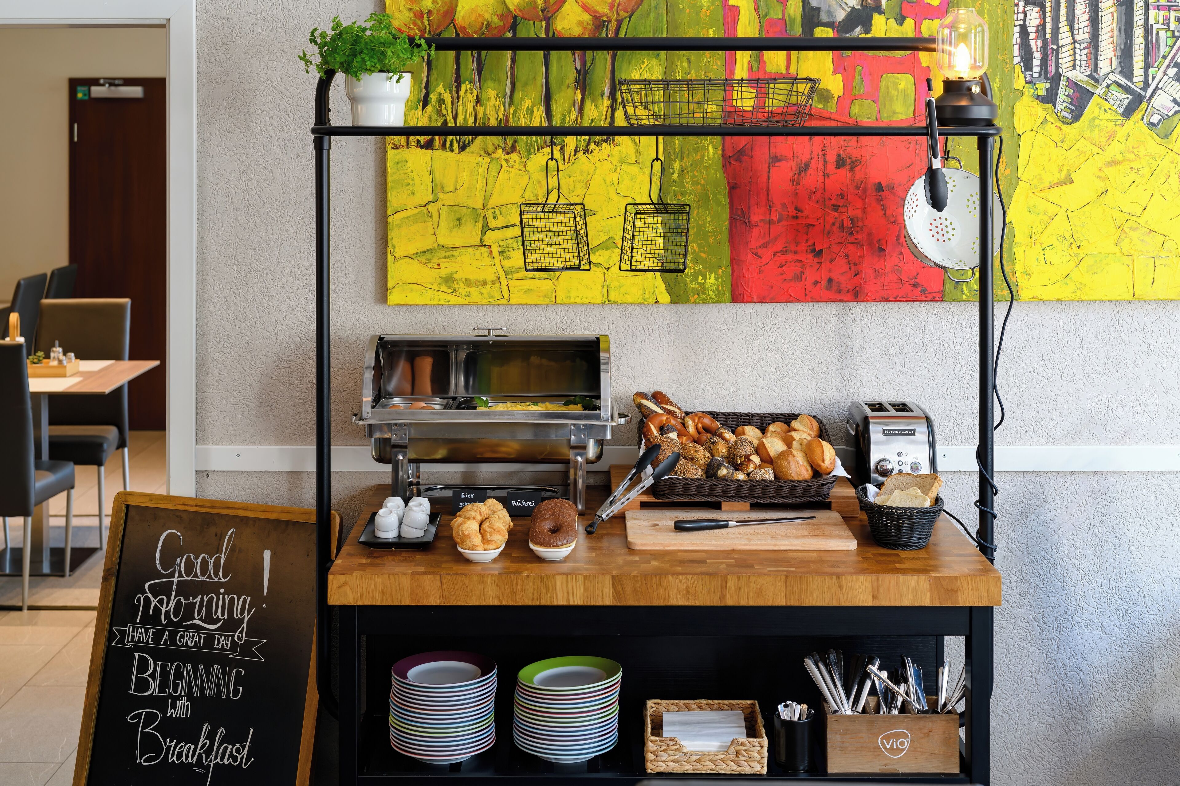 A breakfast bar with a chalkboard sign, a toaster, and a variety of pastries.
