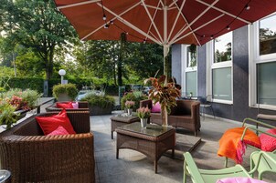 Un patio al aire libre con muebles de mimbre, una mesa de vidrio y un paraguas grande.