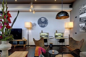 Un moderno vestíbulo de hotel con una televisión de pantalla plana grande, dos zonas de estar con lámparas, una obra de arte colgada en la pared y un candelabro.