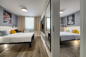 Una habitación de hotel moderna con dos camas, suelo de madera, una escalera y obras de arte en las paredes.