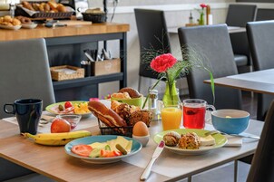 Una mesa de desayuno con diferentes alimentos, una taza de café, un vaso de jugo y un florero.