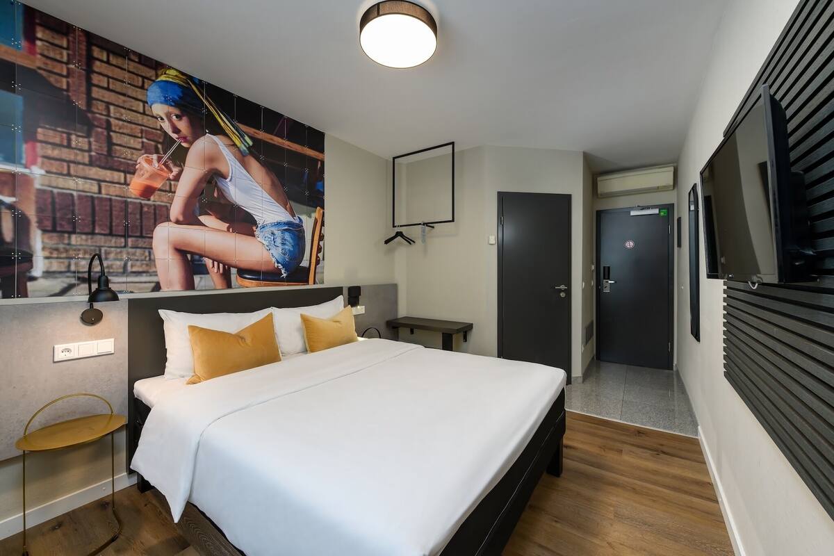 A hotel room with a bed, a wall-mounted TV, a door, and a small table.