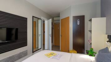 Une chambre d’hôtel avec un lit, un téléviseur fixé au mur, un miroir et une porte donnant sur une autre pièce.
