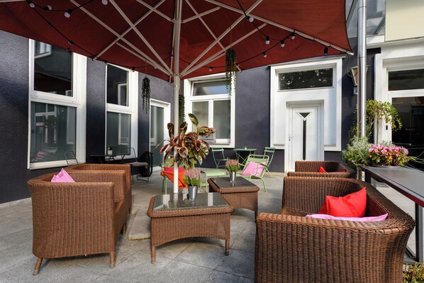 An outdoor seating area with wicker furniture, a glass-top table, and a red umbrella.