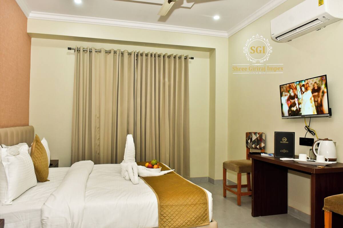 A hotel room with a bed, a desk, a television, and an air conditioning unit.
