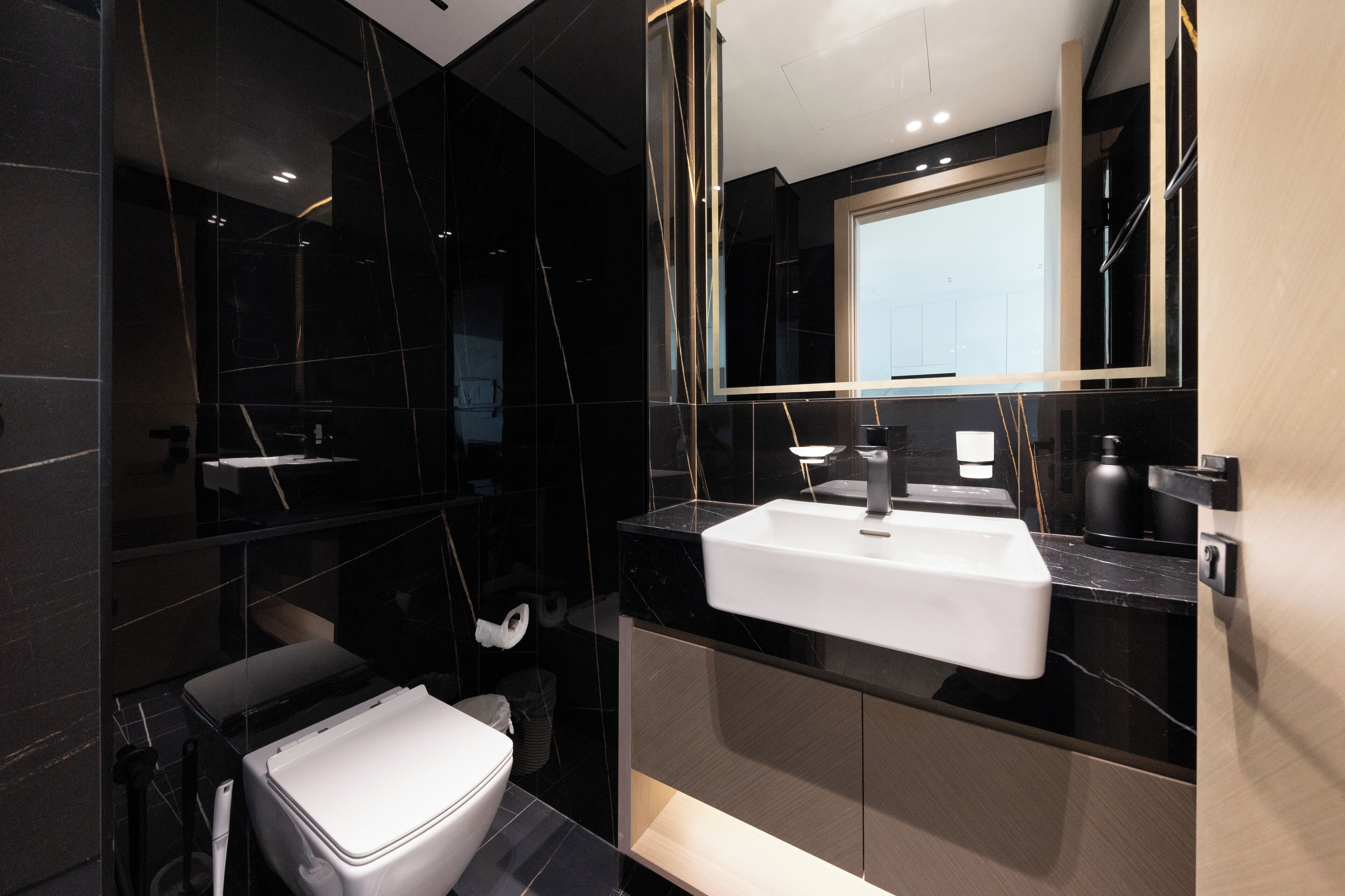 Un bagno moderno con un lavandino bianco, pareti in marmo nero e un grande specchio.
