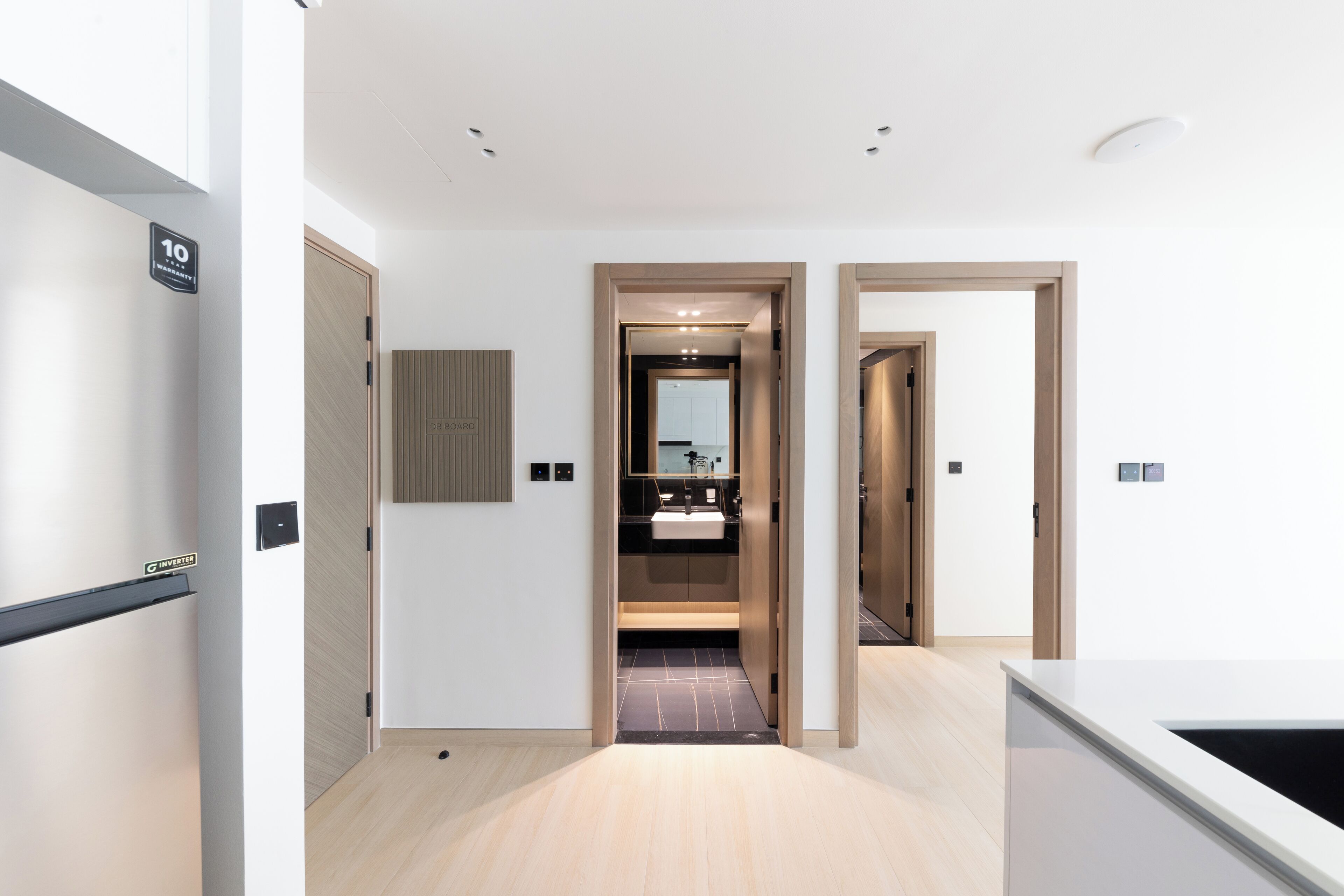 A modern hotel corridor with a wooden floor, a visible bathroom with a sink and mirror, and a door leading to another room.