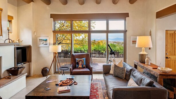 A spacious living room with a large window, a fireplace, a leather sofa, and a coffee table.