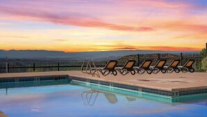 A swimming pool with lounge chairs and a view of the landscape during sunset.