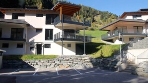 Un edificio moderno con varios balcones, una pared de piedra y un estacionamiento.