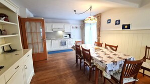 A dining area with a wooden table and chairs, a kitchen in the background, and a chandelier. - Wonderful apartment with views of the slopes (Bad Kleinkirchheim)