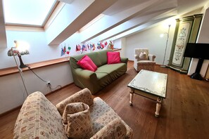 Une pièce confortable de style loft, avec un canapé vert, des fauteuils à motifs, une petite table et un présentoir à drapeaux sur le mur.