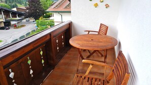 A balcony with a wooden table and chairs, a view of a residential area, and a white wall with decorative items. - Wonderful apartment with views of the slopes (Bad Kleinkirchheim)