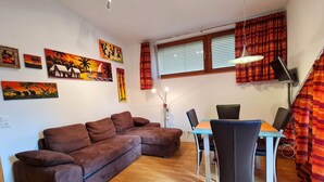 A living room with a brown sectional sofa, a dining table with chairs, and artwork on the walls. - modern apartment with panoramic views (Bad Kleinkirchheim)
