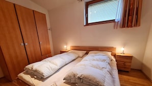 A bedroom with a double bed, wooden wardrobe, bedside tables with lamps, and a window with blinds. - modern apartment with panoramic views (Bad Kleinkirchheim)
