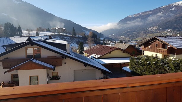 Een bergdorpje met traditionele houten huizen, een heldere lucht en besneeuwde heuvels op de achtergrond.