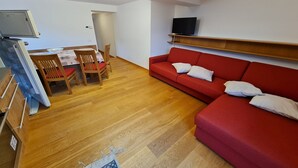 Een woonkamer met een rode bank, een houten eettafel, stoelen en een televisie op een plank.