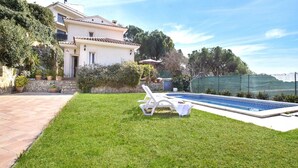 Una casa con piscina, césped y un muro de piedra.