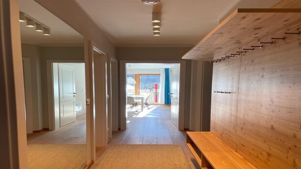Un pasillo con un banco de madera, una escalera y vistas a un espacio exterior con una mesa y sillas.