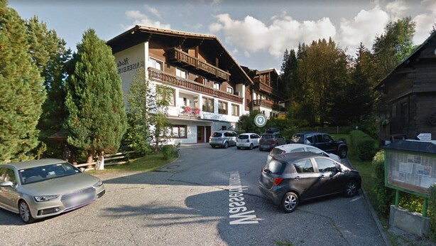 A hotel with a traditional Alpine architectural style, featuring balconies and a mountain view.