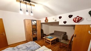 A cozy room with a bed, a wooden wardrobe, a sofa, a small table, and a mirror.