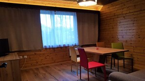 A cozy room with a wooden floor, a dining table with chairs, a television, and a window with curtains. - Nature & Ski Retreat in Bad Kleinkirchheim (Bad Kleinkirchheim)