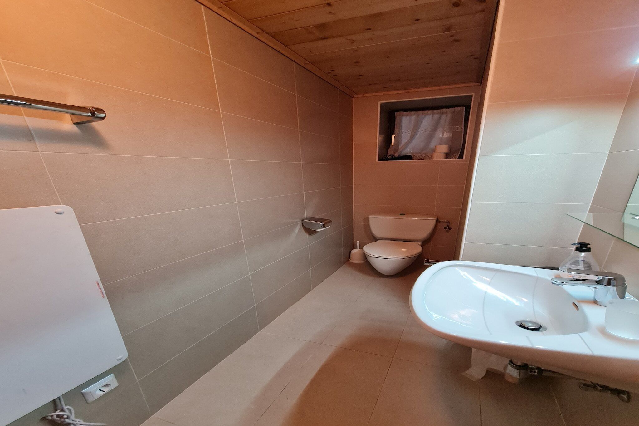 Ein Badezimmer mit einem weißen Waschbecken, einer Toilette und einem Fenster mit Vorhang.
