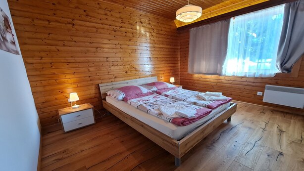 A wooden-paneled bedroom with a bed, bedside lamps, and a window with curtains. - Nature & Ski Retreat in Bad Kleinkirchheim (Bad Kleinkirchheim)