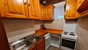 A kitchen with wooden cabinets, a stainless steel sink, a white stove, and a window with a white curtain. - Nature & Ski Retreat in Bad Kleinkirchheim (Bad Kleinkirchheim)