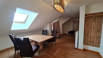 Een moderne loft slaapkamer met dakraam, houten vloeren, een eethoek met tafel en stoelen, en een inbouwkast.