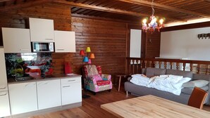 Ett mysigt rum inrett som en stuga, med träpanel på väggarna, ett matbord, en soffa och en färgglad lampa.