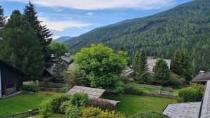 A rural setting with a house surrounded by a wooden fence, a large tree, and a mountain backdrop. - Apartment with mountain views (Bad Kleinkirchheim)